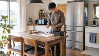杢ブラウンのスウェットを着た眼鏡の父親がキッチンでレシートの束を仕分けている