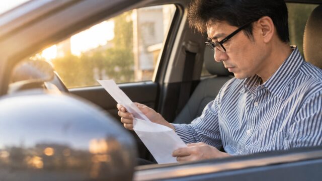 車の中で給与明細を見て社会保険料の変化に気づく眼鏡のパパ