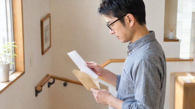 眼鏡をかけた男性が封筒から出した無地の紙を読む・年末調整の還付を確認するイメージ