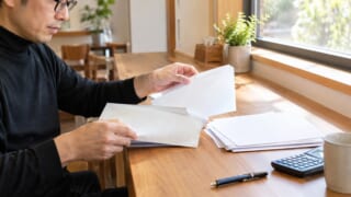 窓際のカウンターで届いた保険の書類を仕分ける眼鏡のパパ